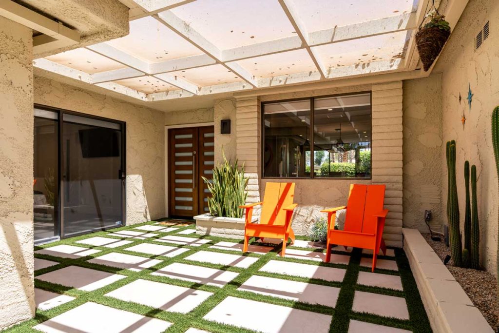 entryway with pavers and grass, two orange chairs and covered patio