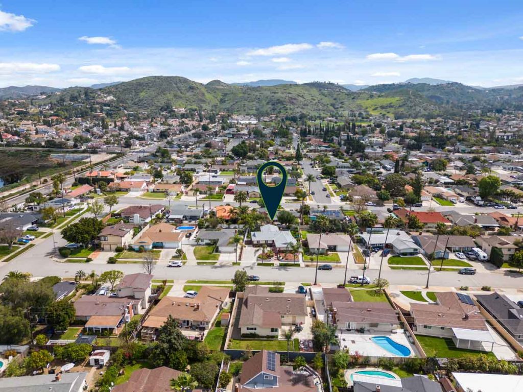 aerial view of neighborhood with hills in the background and arrow pointing to house for sale