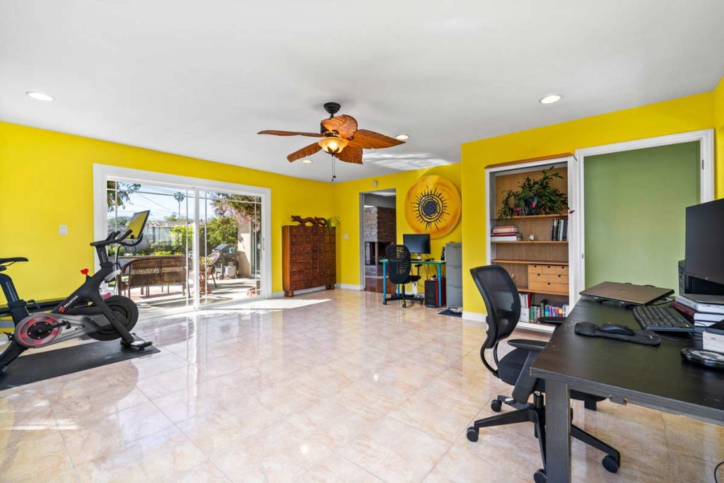 large room with yellow walls, desk and workout equipment, with sliding glass doors leading to the backyard