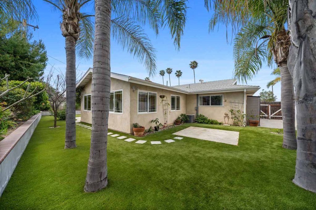 backyard with a lot of grass, palm trees and house