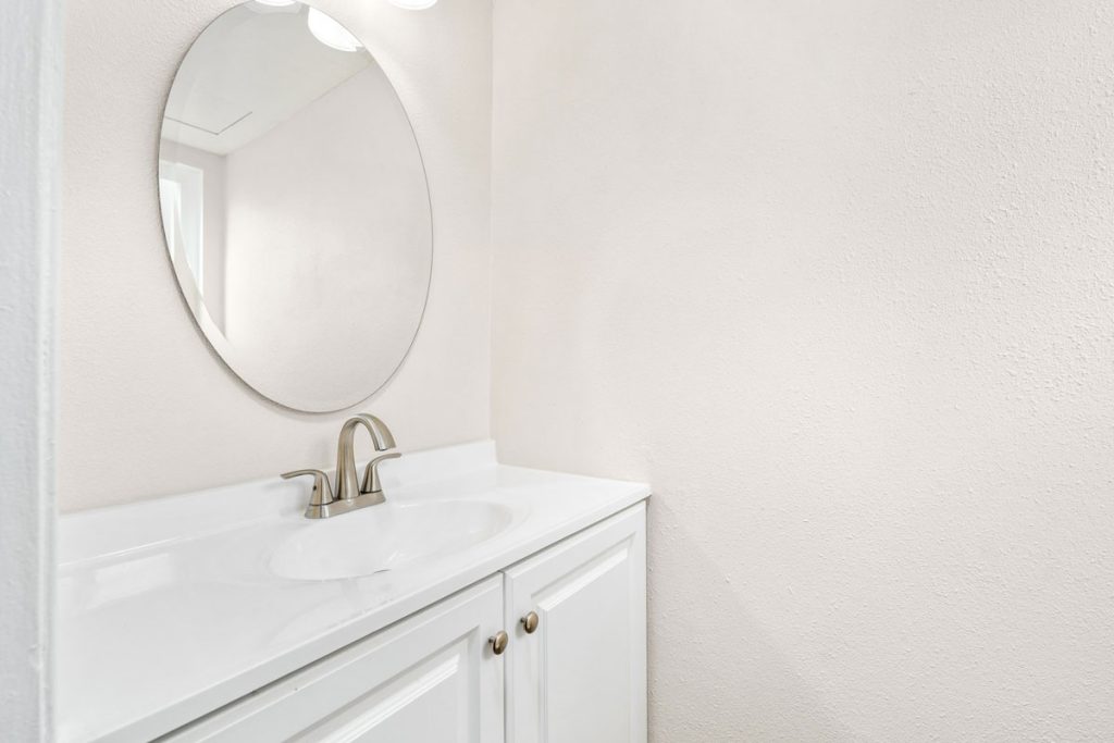 simple clean bathroom with white vanity, circle mirror and white walls