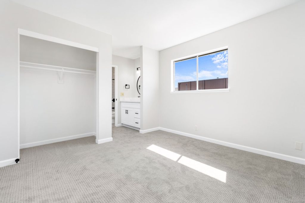 empty bedroom with white walls, window and entry to a bathroom