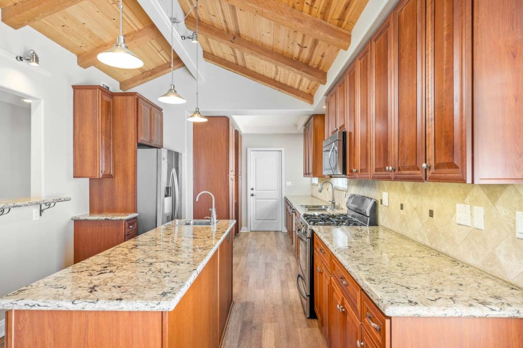 vaulted wood planked ceiling in a galley kitchen with wood cabinets and granite