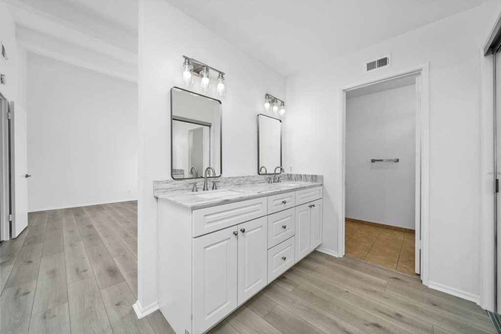 master bathroom with double sinks, open to bedroom with a small toilet room.