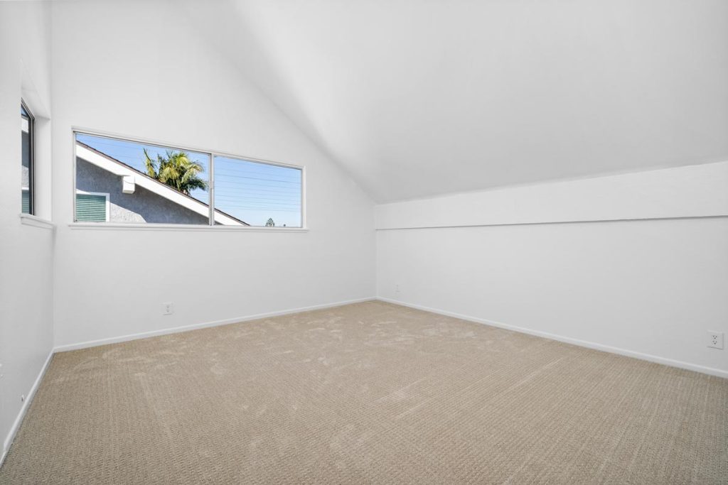 large empty carpeted oom with white walls and windows