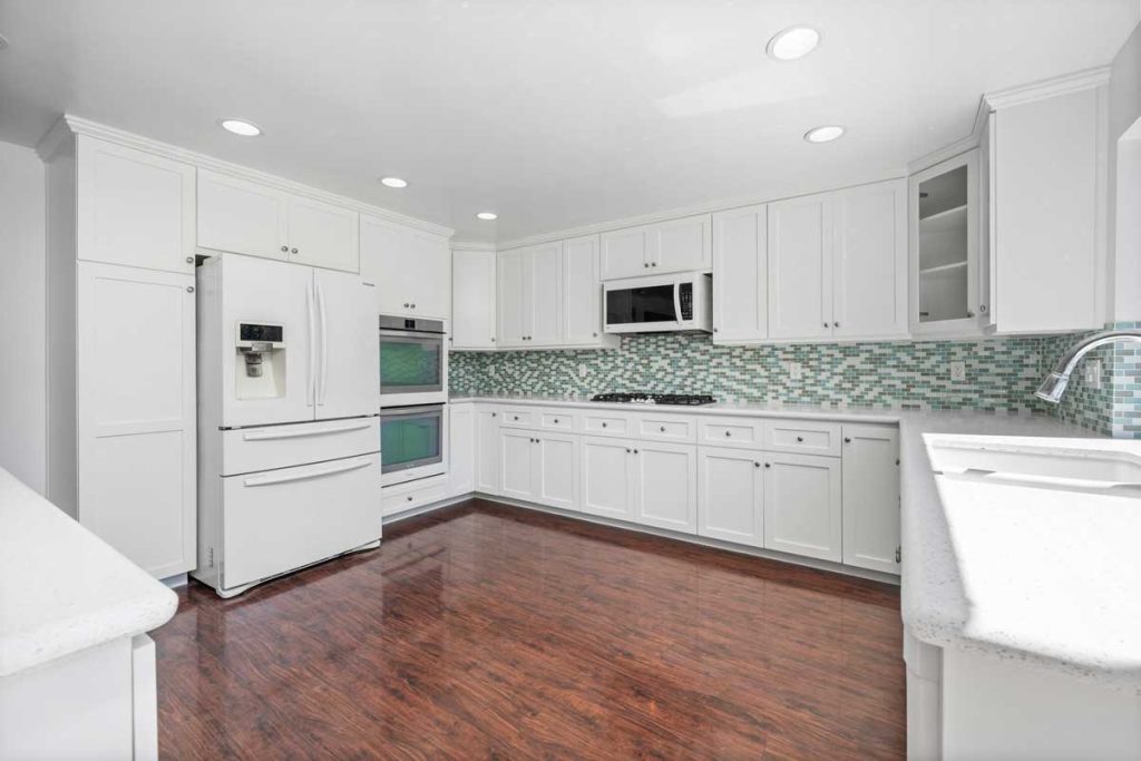 white kitchen cabinets and refrigerator with teal glass backsplash