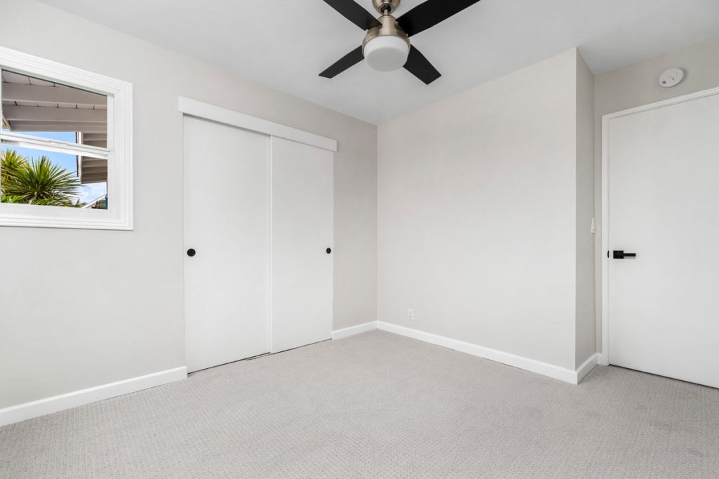 empty bedroom with neutral paint and carpet, window, closet doors and ceiling fan