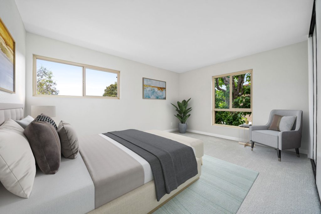 staged bedroom with bed and chair, and windows looking outside