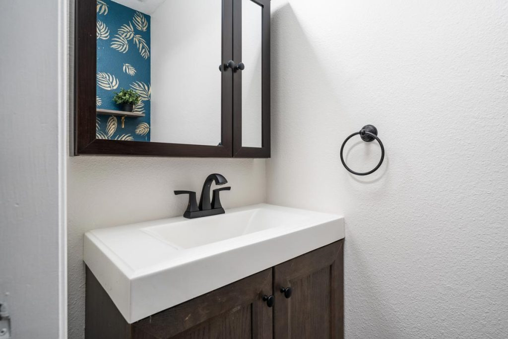 bathroom showing mirror over vanity with dark wood and white counters and black faucet