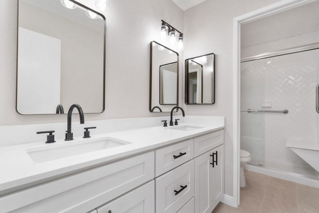 bathroom with white dual vanities and a separate room for toilet and shower.