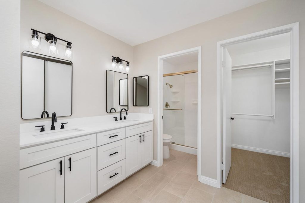 master bathroom with double white vanity and doors leading to walk-in closet and toilet