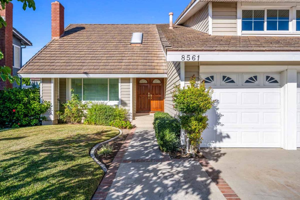 exterior entrance and walkway to home showing front winder, wooden double doors, grass, bushes and garage door