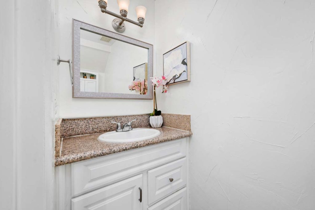 bathroom vanity showing white cabinetry, tan stone countertops a mirror and light fixture