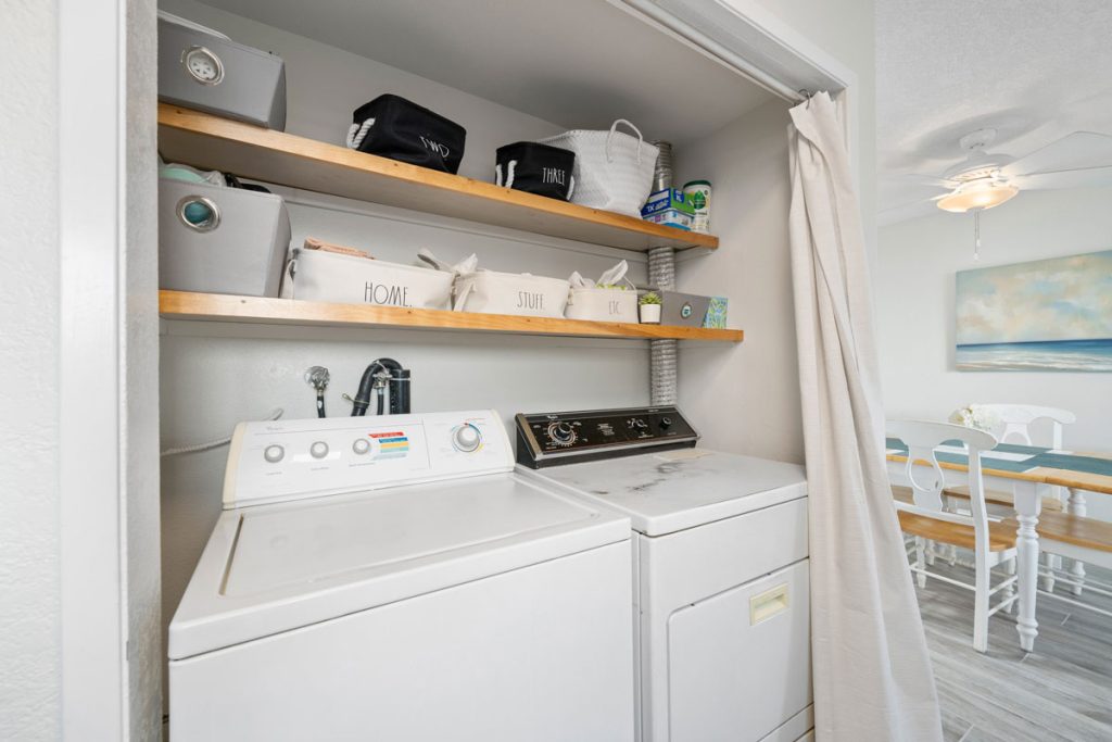 laundry space showing washer and dryer with shelves above and curtains to close off