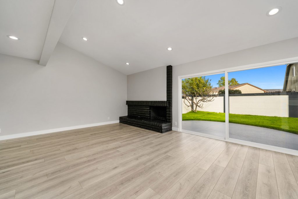 empty living room with light colored hard flooring, black fireplace and large sliding glass door leading to backyard