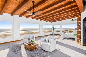 wall of windows viewing sand and ocean, wood ceiling with beams