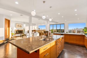 warm wood cabinets in kitchen with dark floors and counters with wall of windows looking out to ocean