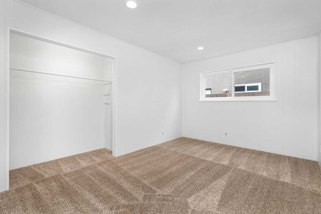 empty bedroom with white walls, tan carpet and a small window