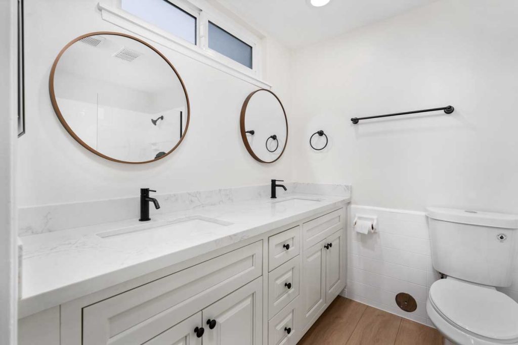 updated bathroom showing white double vanity, two circular mirrors, and a toilet