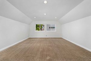 empty bedroom with white walls, tan carpet and a window