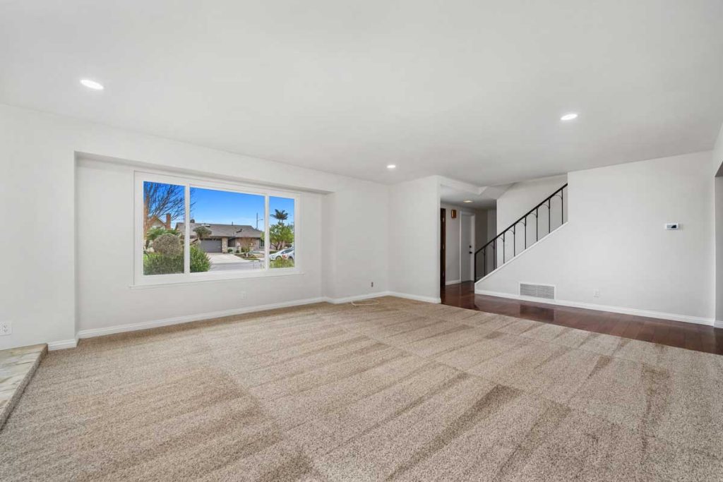 empty living room showing carpeted space with window, stairs and the front door in the background