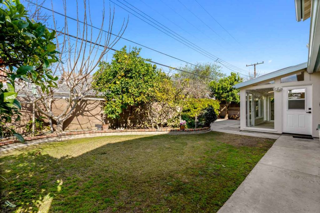 backyard with grassy area, plants surrounding the perimeter, and the house in the background