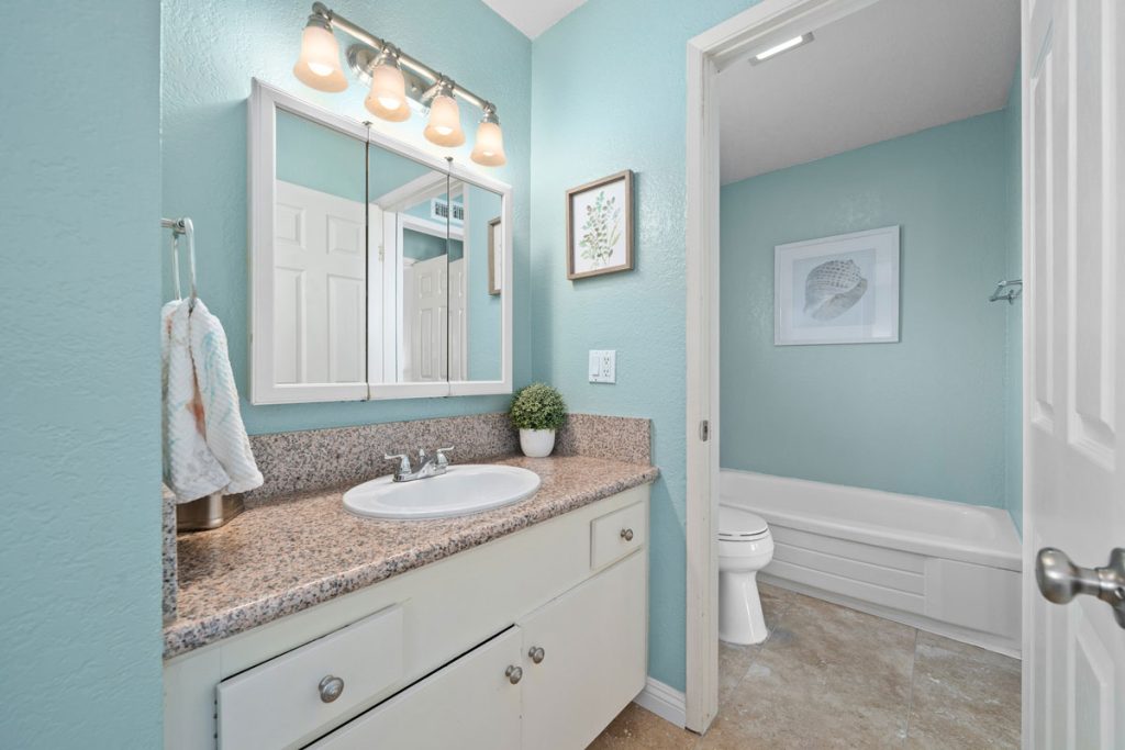 master bathroom with light blue walls, white cabinet vanity, tan counters, and a door leading to the toilet and bath/shower space