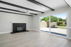 empty living room with neutral floors, black fireplace and brown beams on the ceiling.