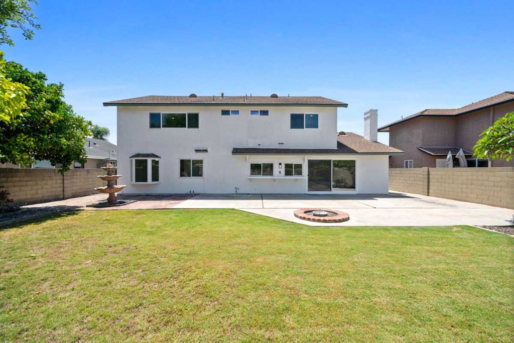view of backyard facing towards the house showing grass firepit and fountain.