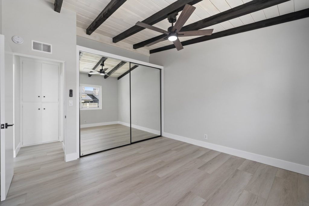 empty bedroom with dark ceiling beams and wood plank looking flooring and mirrored closet door