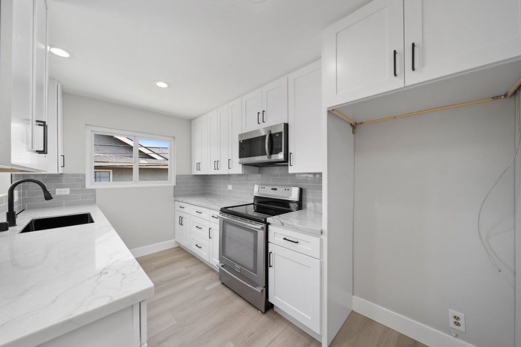 updated kitchen with white cabinets stone counters, stainless range and a window