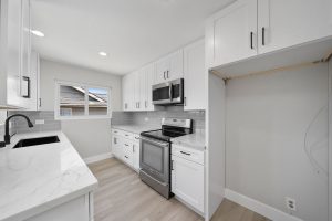 updated kitchen with white cabinets stone counters, stainless range and a window