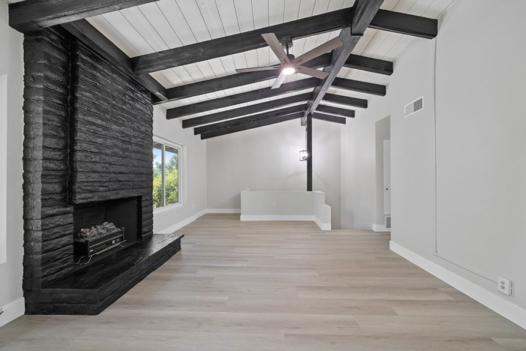 empty living room with black fireplace, wood-looking floors, dark ceiling beams and neutral wall paint