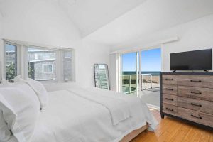 bedroom showing bed with white bedding, sliding glass door to patio overlooking the beach