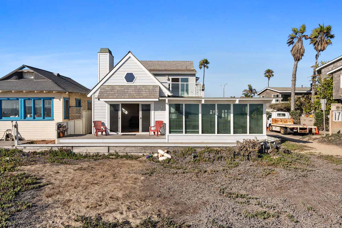 view of home on the sand with blue skies and palm trees in the background