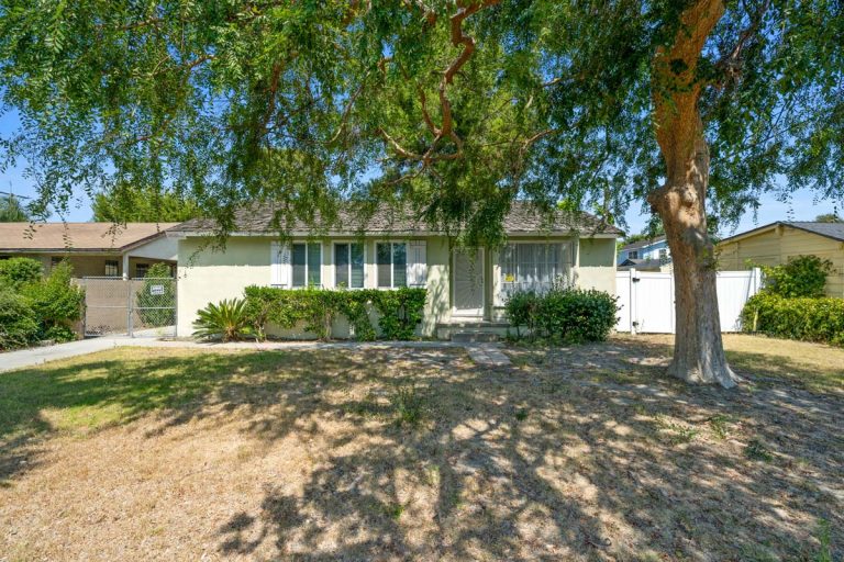 front view of exterior of home showing light colored paint, bushes and large tree