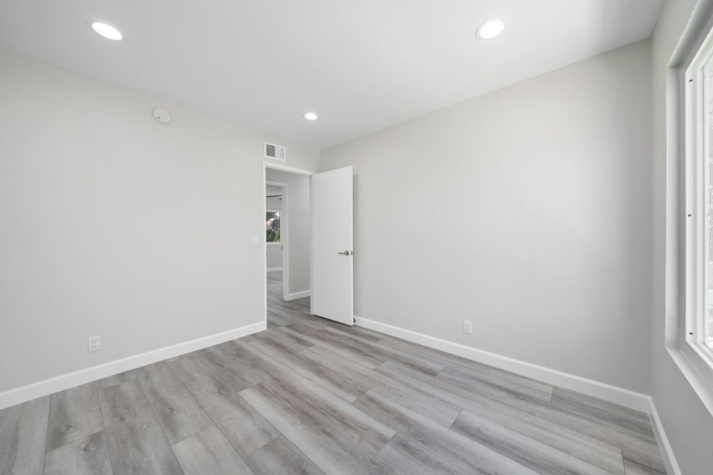neutral empty bedroom with plank floors and recessed lights