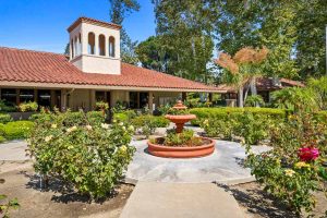 walkway to community center with a fountain in the foreground and a spanish-style building in the background.