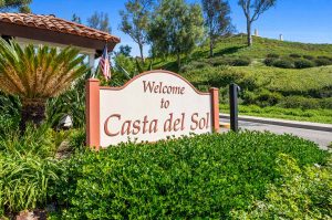entry sign to community saying Welcome to Casta del Sol with bushes and trees in background.