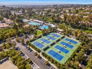 aerial view of mission viejo showing tennis courts, pools, trees, homes, and cars in parking spaces.