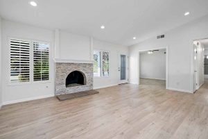 white walls in the living room with laminate floors, windows, and a fireplace with brick surround.