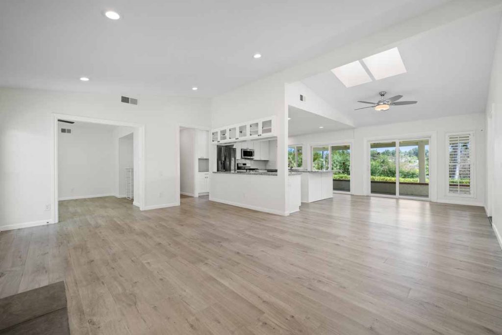 bright open living room opening up to the kitchen showing a wall of glass windows and doors, laminate flooring, and ceiling fan.