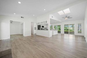 bright open living room opening up to the kitchen showing a wall of glass windows and doors, laminate flooring, and ceiling fan.