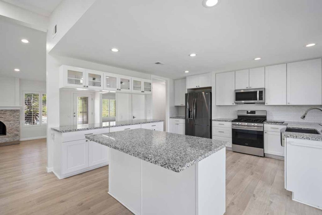 white kitchen with granite countertops, stainless appliances and an island in the center.
