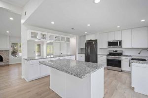 white kitchen with granite countertops, stainless appliances and an island in the center.