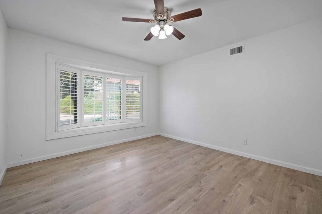 empty bedroom with laminate floors, a large windows and a ceiling fan