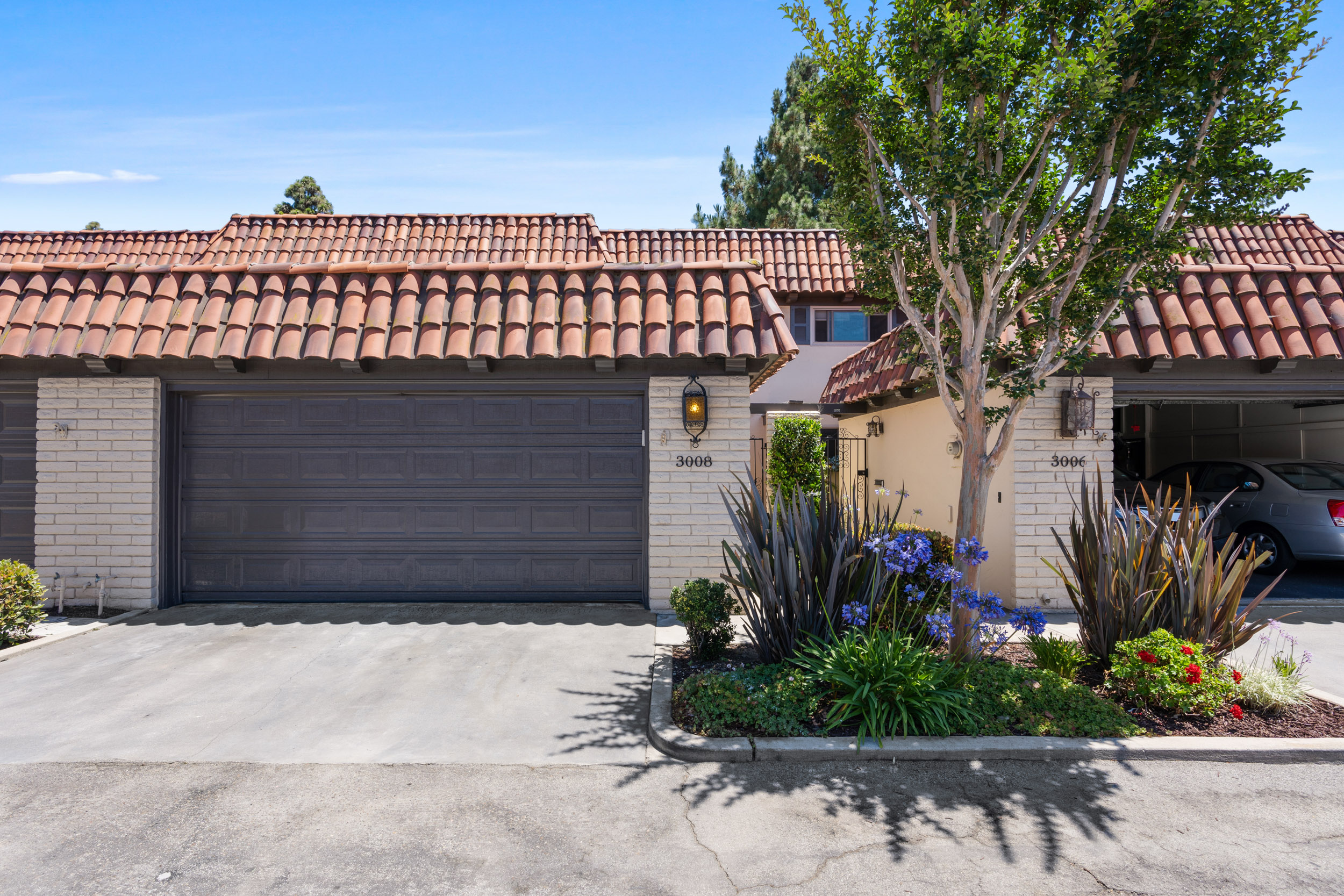exterior of home for sale in costa mesa, showing cream colored stucco, brown garage door and terracotta roof tiles