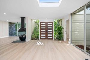 inside view of mid-century modern style front doors with windows surrounding the door and the wall next to it. Lots of light and greenery from the outside.