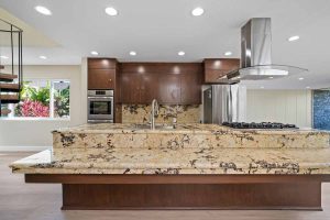 updated kitchen with a large two-tiered island made of brown toned wood cabinetry and tan/brown granite.