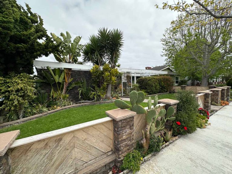 exterior view of home for sale showing angled wood slatted fence, grass and a lot of shrubbery.